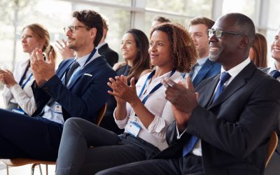 A group of business people clapping at a conference, noticed by online business professionals.