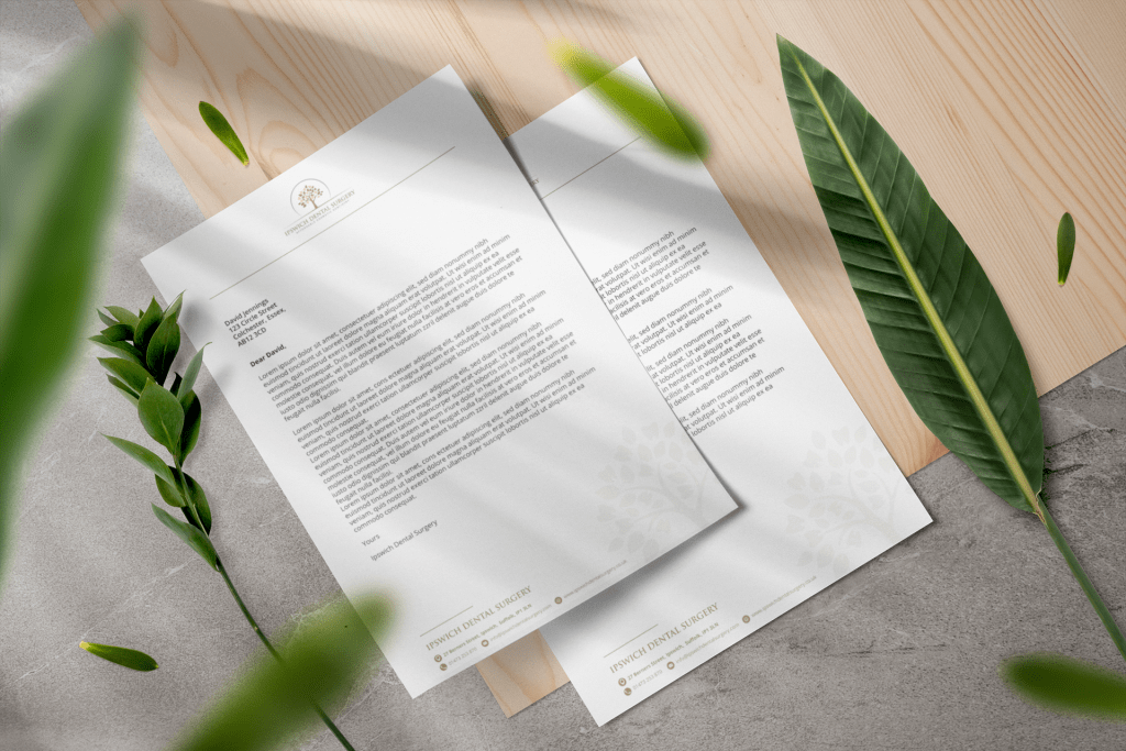 Two letterheads on a wooden table with green leaves.