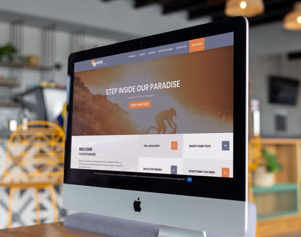 An imac on a desk displaying a travel website homepage with a 'step inside our paradise' headline.