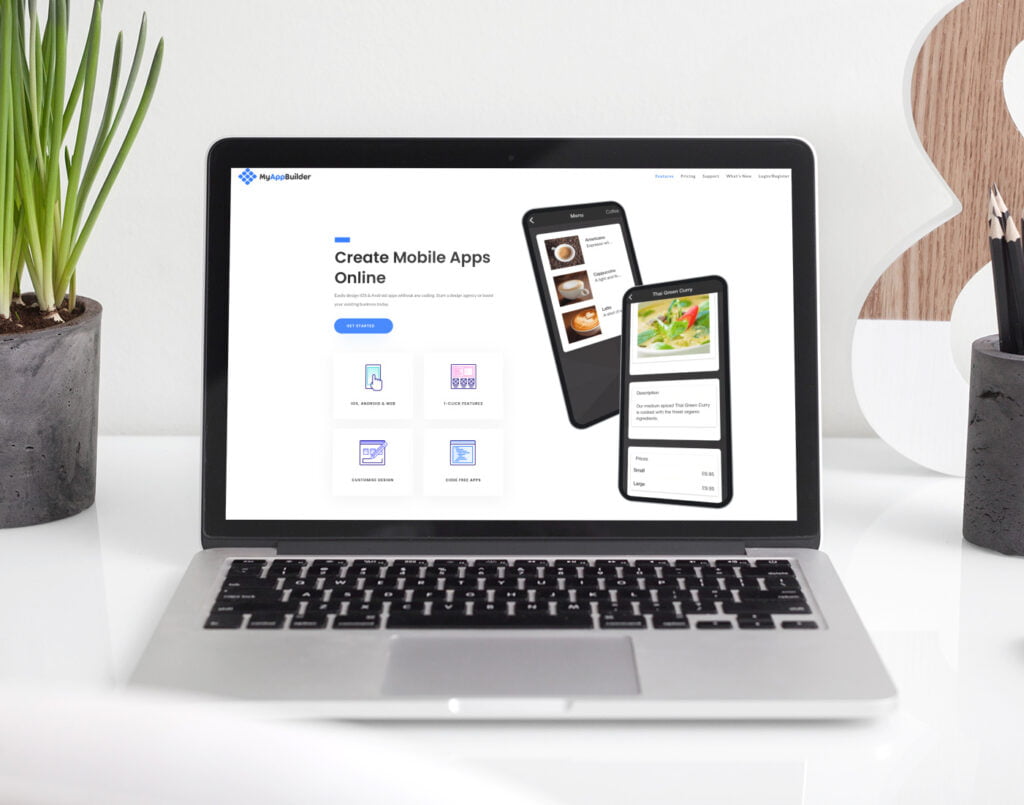 A laptop on a desk displaying a mobile app creation website, flanked by a tablet and smartphone showing the app interface, with indoor plants on either side.